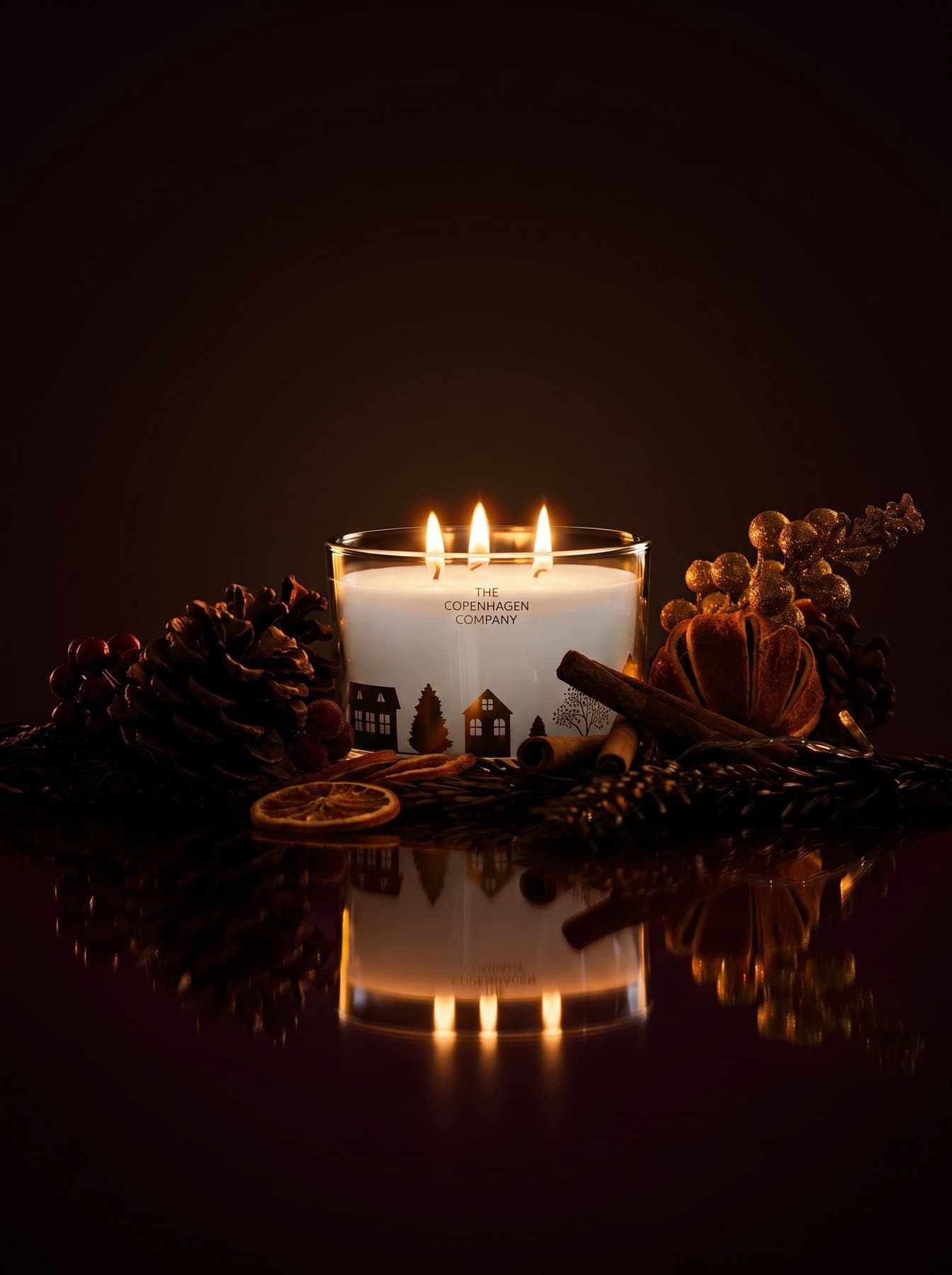 A three-wick Christmas candle among pine, dried orange and berries