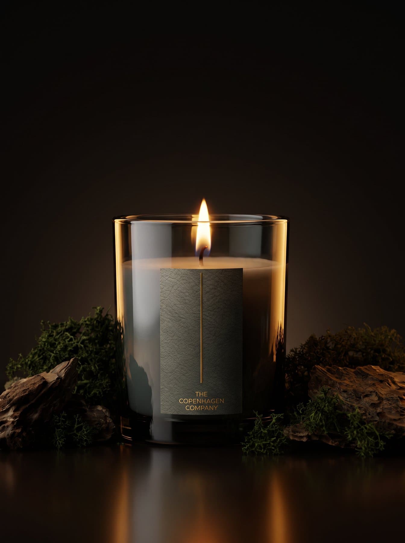 A lit Oud candle in dark glass on a bed of moss