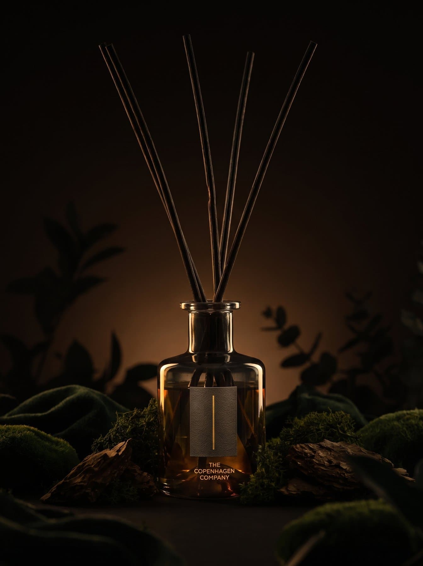 An Oud diffuser on moss, ferns behind