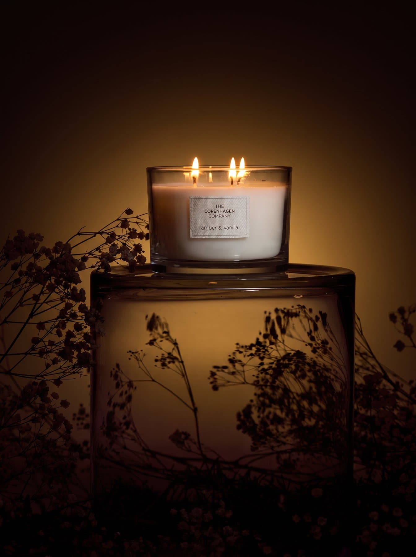 A Signature candle on a glass block, dried meadow grasses behind it