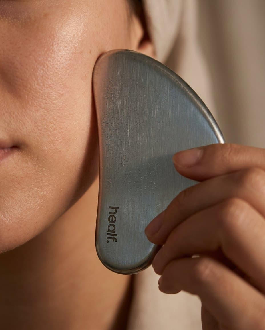 The steel gua sha against a cheek